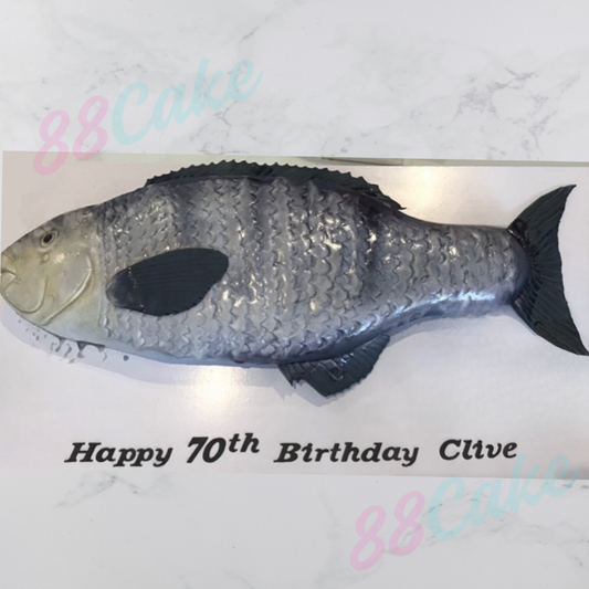 Fish-shaped birthday cake with 'Happy 70th Birthday Clive' text on a marble background