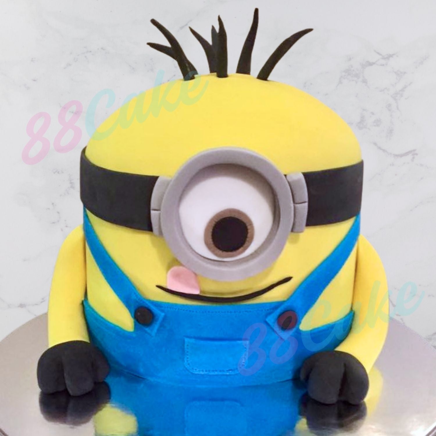 Minion-themed cake with yellow face, blue overalls, and black hair 