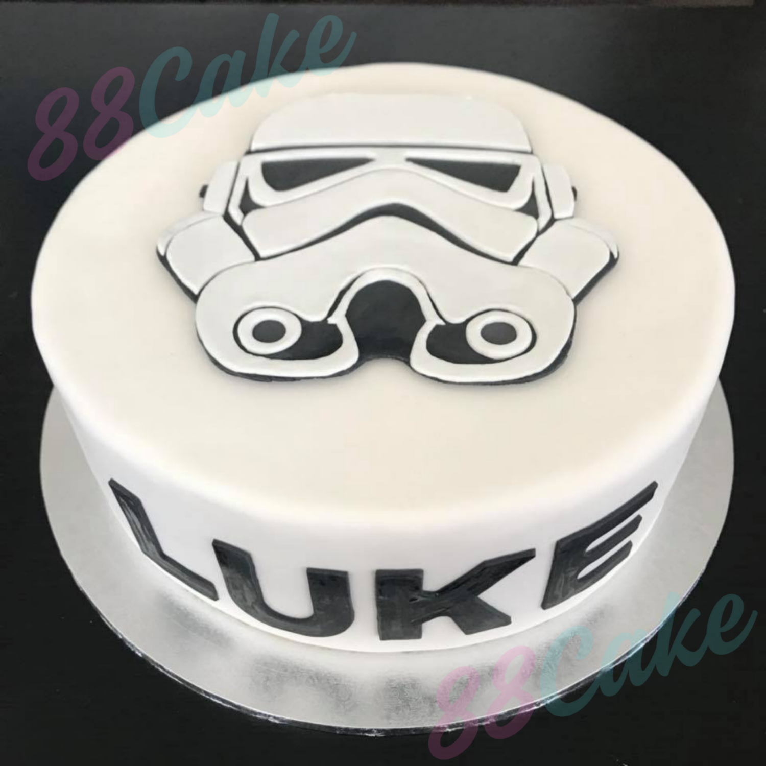 Round cake with a stormtrooper design and the name 'Luke' on a black background.